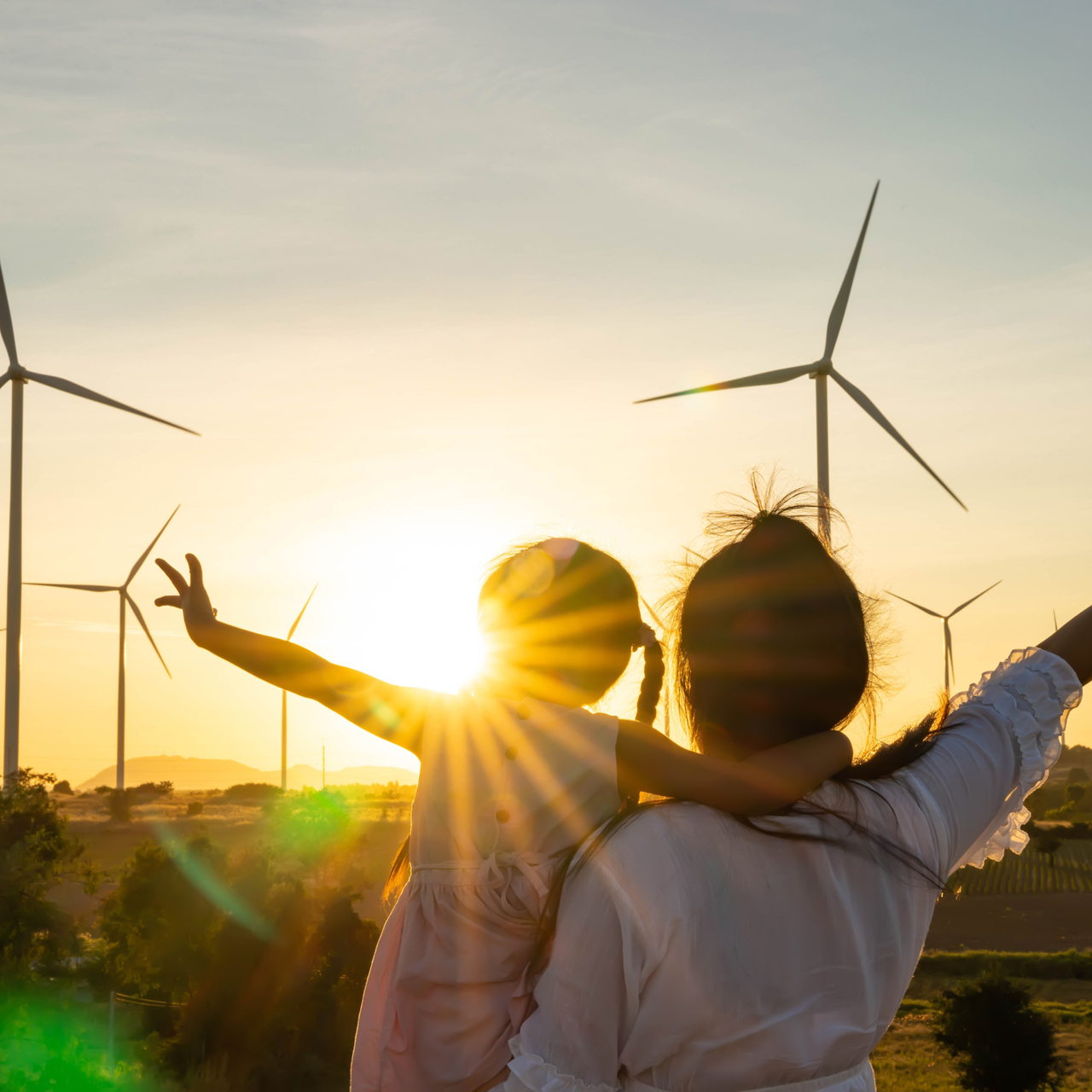 Women And Female Child Cuddling In Front Of Wind Turbines
