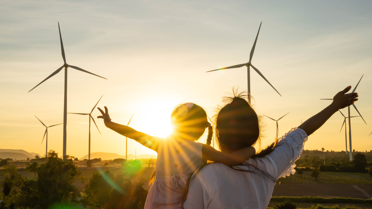 Women And Female Child Cuddling In Front Of Wind Turbines