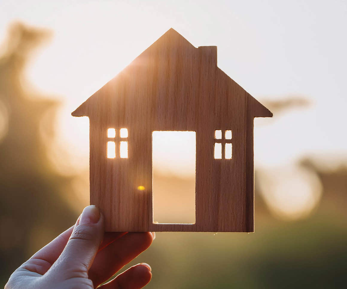 Miniature house held in a persons hand against a bright backdrop