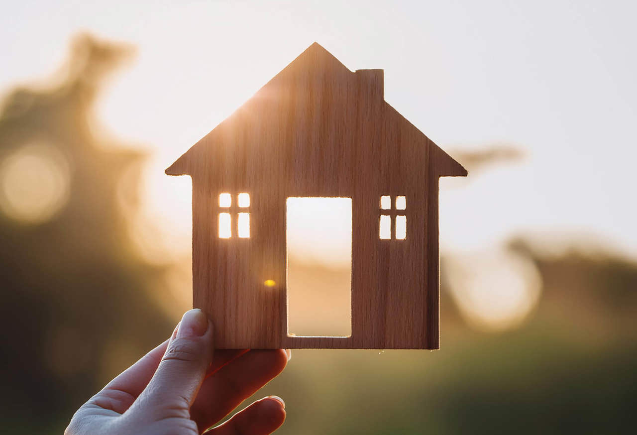 Miniature house held in a persons hand against a bright backdrop
