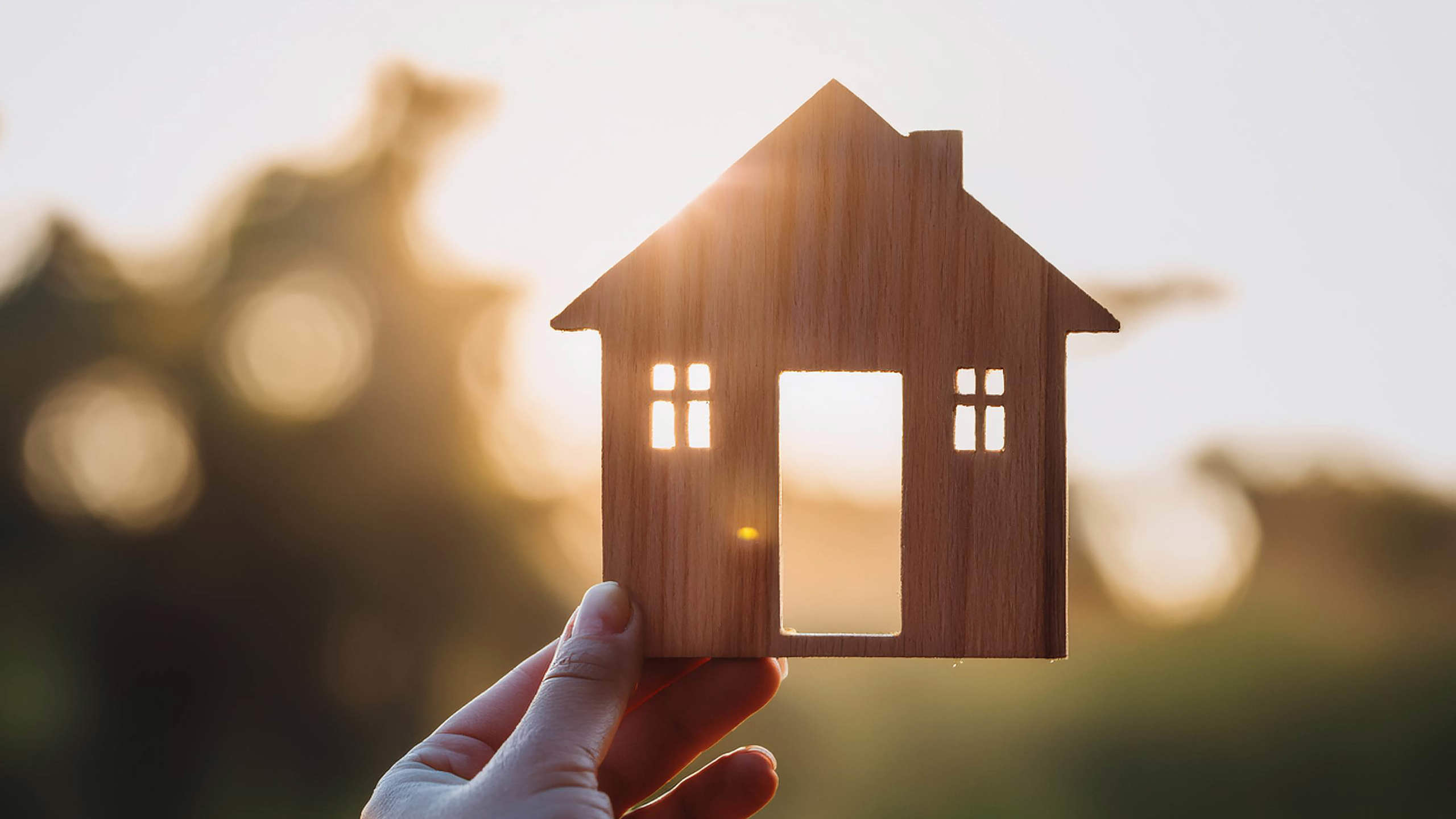 Miniature house held in a persons hand against a bright backdrop