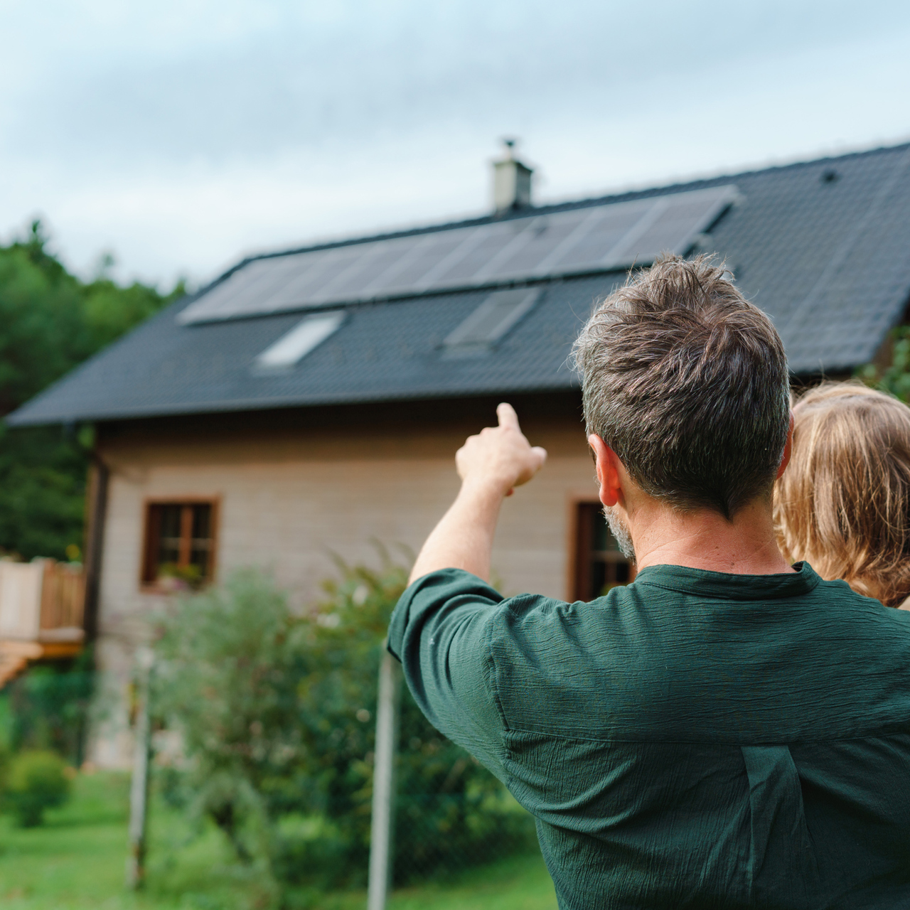 Man And Girl Pointing At Solar Panels On Home