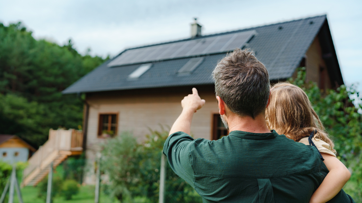Man And Girl Pointing At Solar Panels On Home