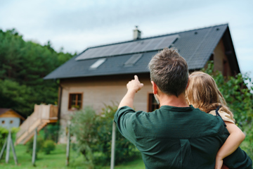 Man And Girl Pointing At Solar Panels On Home
