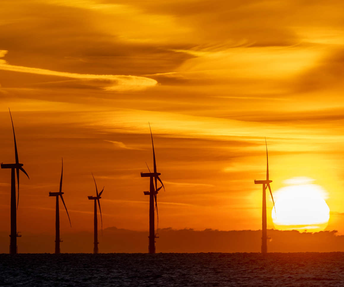 Offshore wind turbines against a an orange sky at sunset