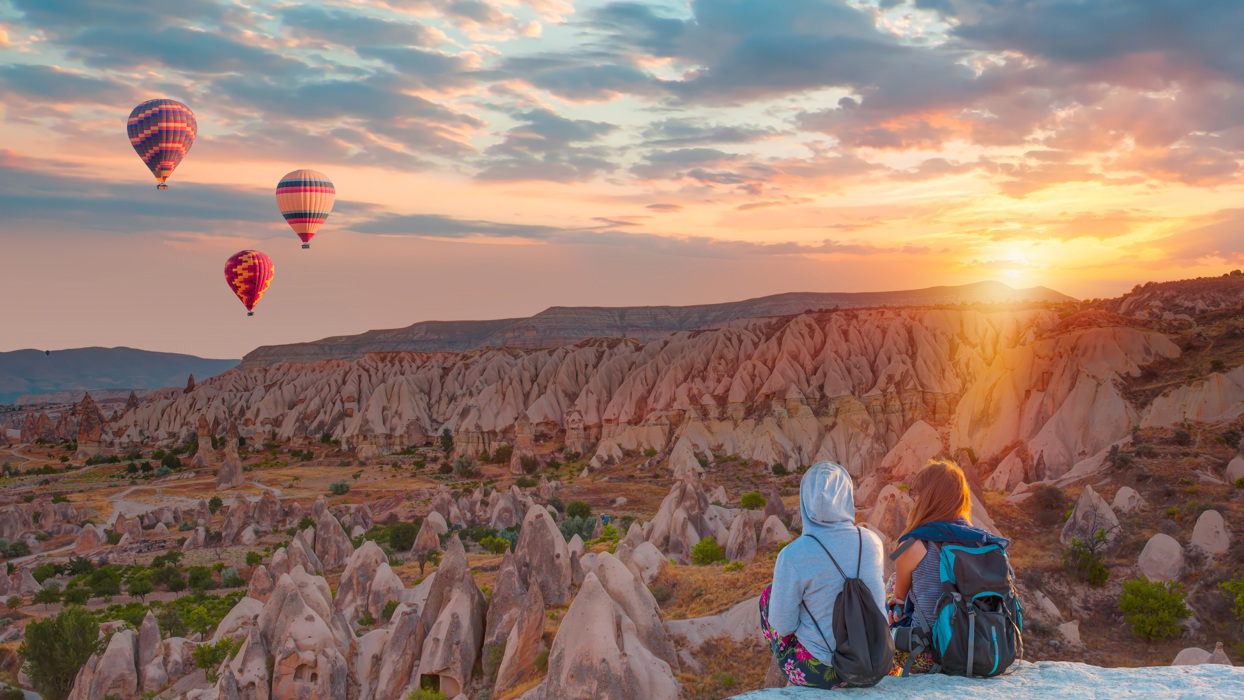 Two people looking at hot air balloons floating above rocky landscape