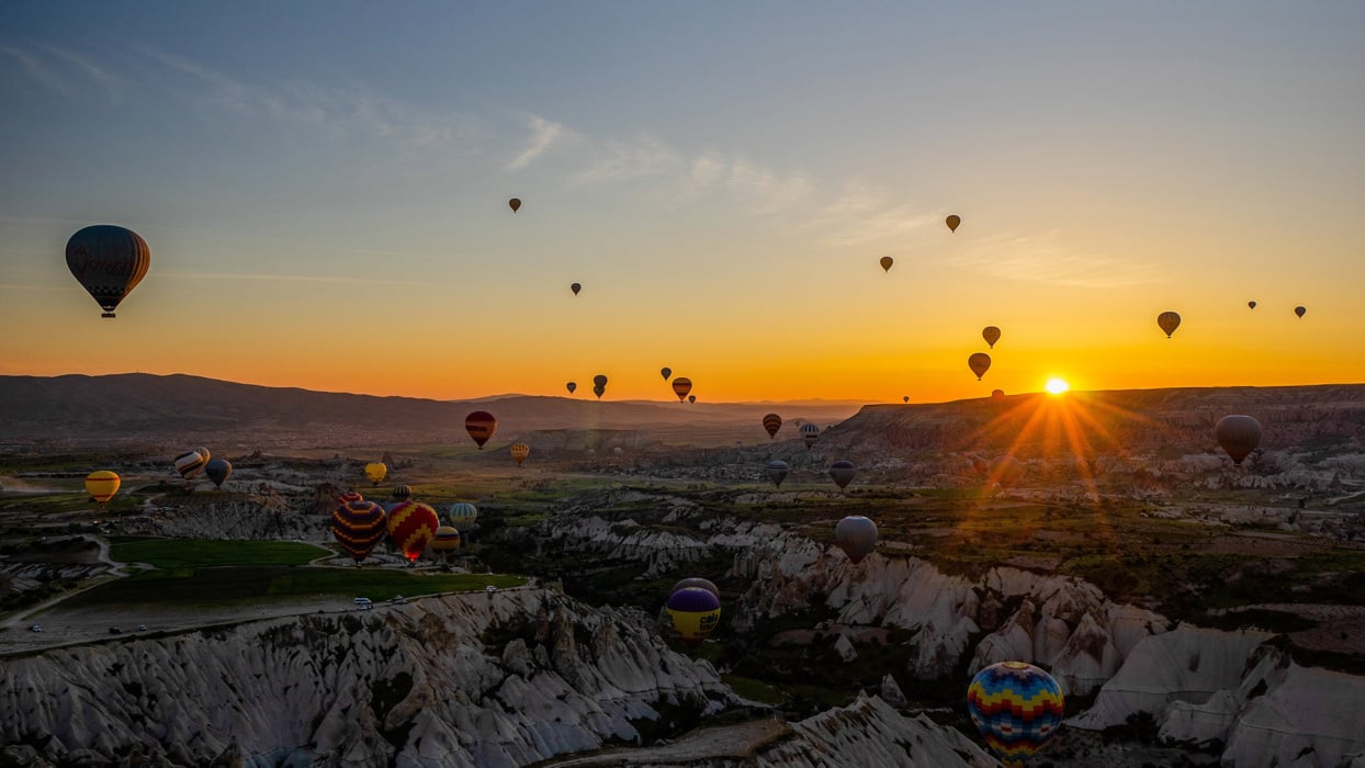 Hot air balloons floating over valleys during sunset