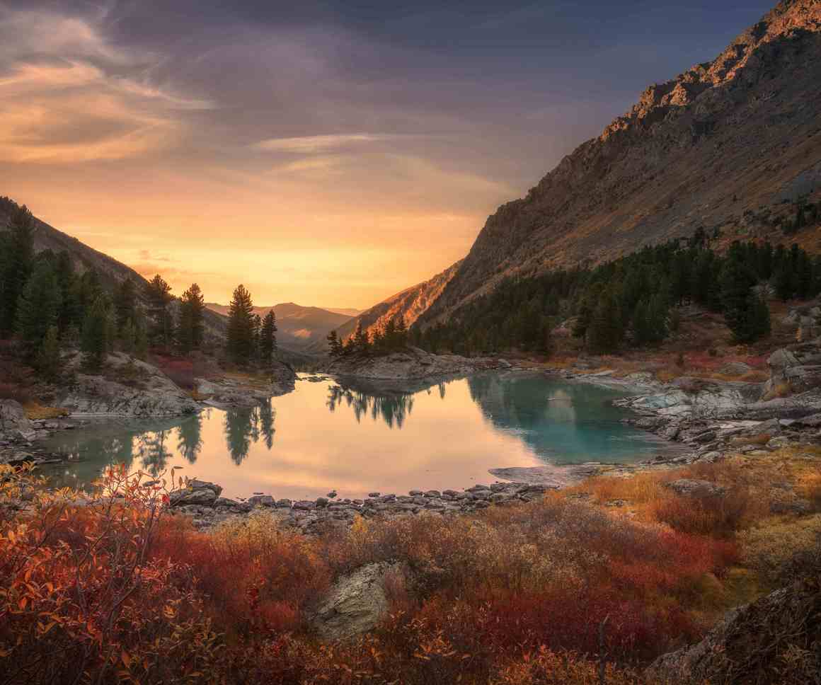 Landscape of a valley in between two mountains with the sun setting, a lake and autumnal foliage