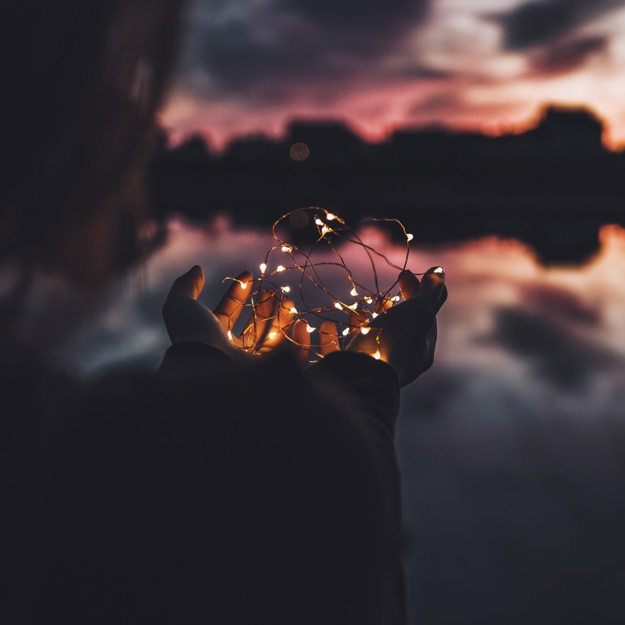 Person Holding Fairy Lights Against An Atmospheric Sky