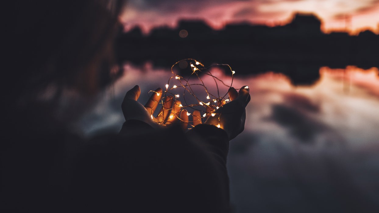 Person Holding Fairy Lights Against An Atmospheric Sky