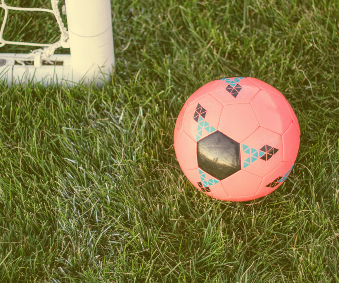 Football on a pitch next to a goal post